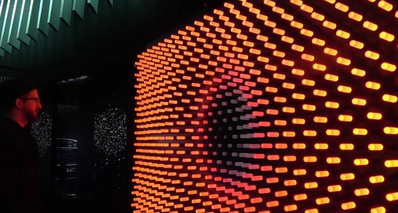 A curved kinetic light wall with rows of illuminated orange lights.