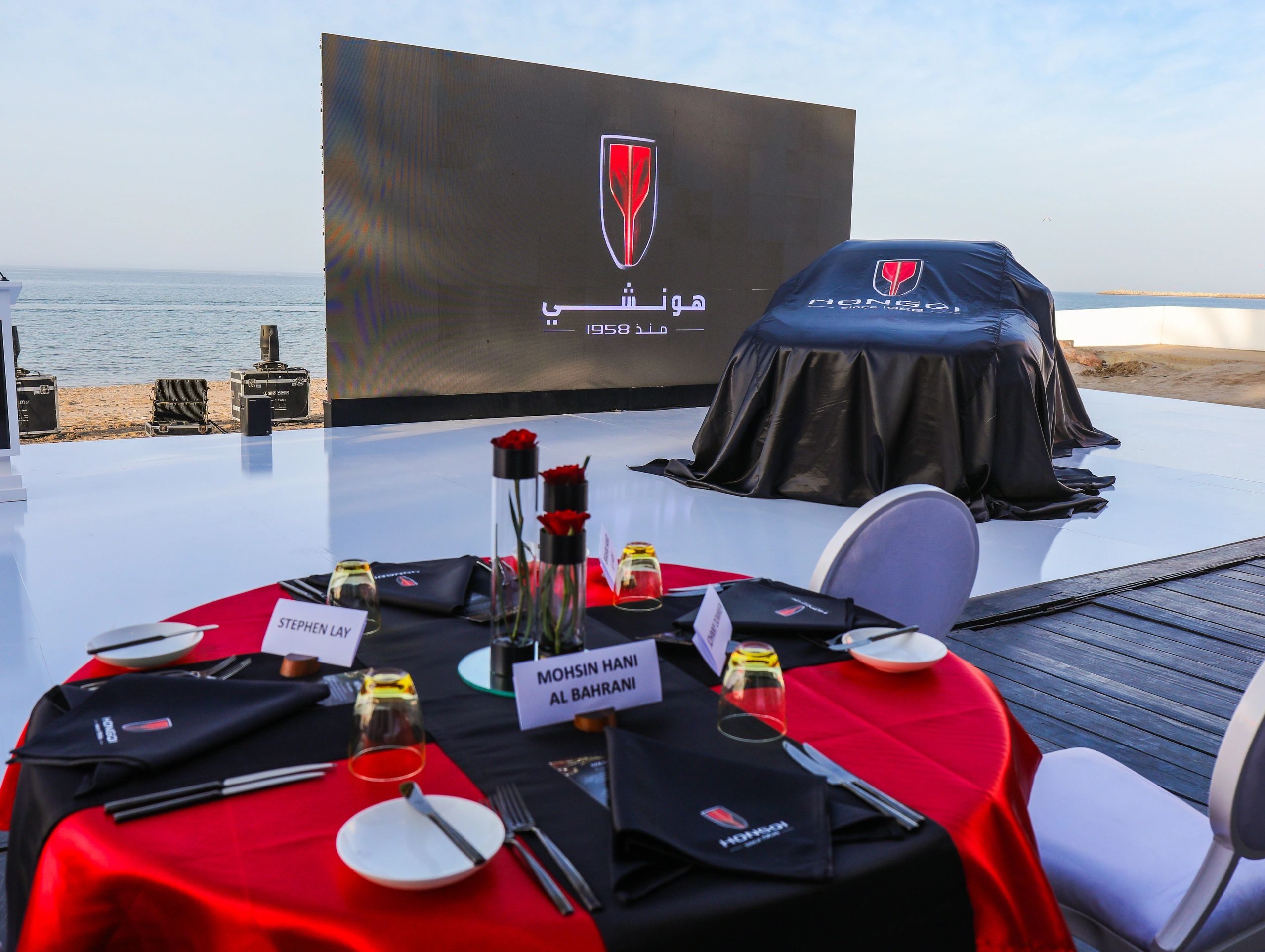 Hongqi coastal event with a covered vehicle, branded stage and guest tables