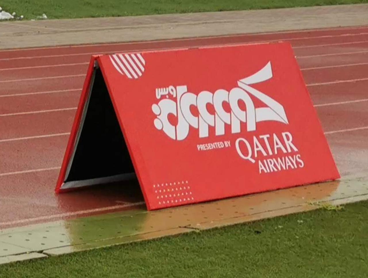 A freestanding Qatar Airways-branded A-board beside an athletics track.