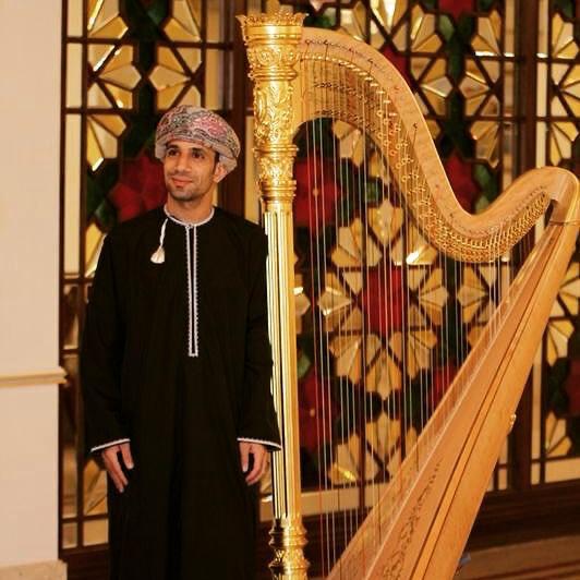 A harpist beside a gold harp in an indoor venue.